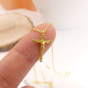 Puede incluir: Un collar de cadena dorada con un peque&ntilde;o colgante de cruz dorada que presenta una figura detallada de Jesucristo.
