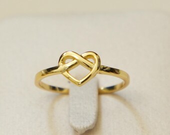 May include: A gold ring with a heart-shaped design. The ring is on a white display stand.