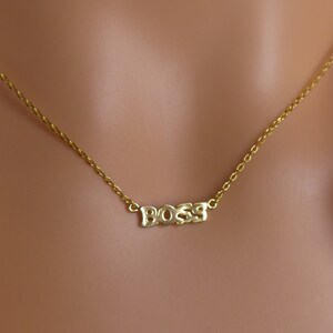 May include: A gold chain necklace with the word "BOSS" spelled out in block letters.