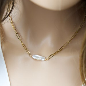 May include: A gold chain necklace with a single large white baroque pearl pendant.