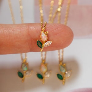 May include: Four gold necklaces with a delicate flower pendant featuring a white opal stone and green accents.