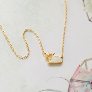 May include: A gold chain necklace with a white enamel cloud pendant and a small sun charm.
