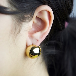 May include: A pair of gold-toned ball stud earrings. The earrings are round and have a smooth, shiny finish.