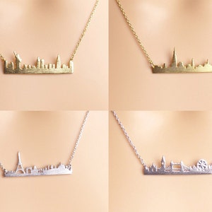 May include: Four necklaces with city skyline pendants. The top left necklace features a gold New York City skyline pendant. The top right necklace features a gold London skyline pendant. The bottom left necklace features a silver Paris skyline pendant. The bottom right necklace features a silver London skyline pendant.