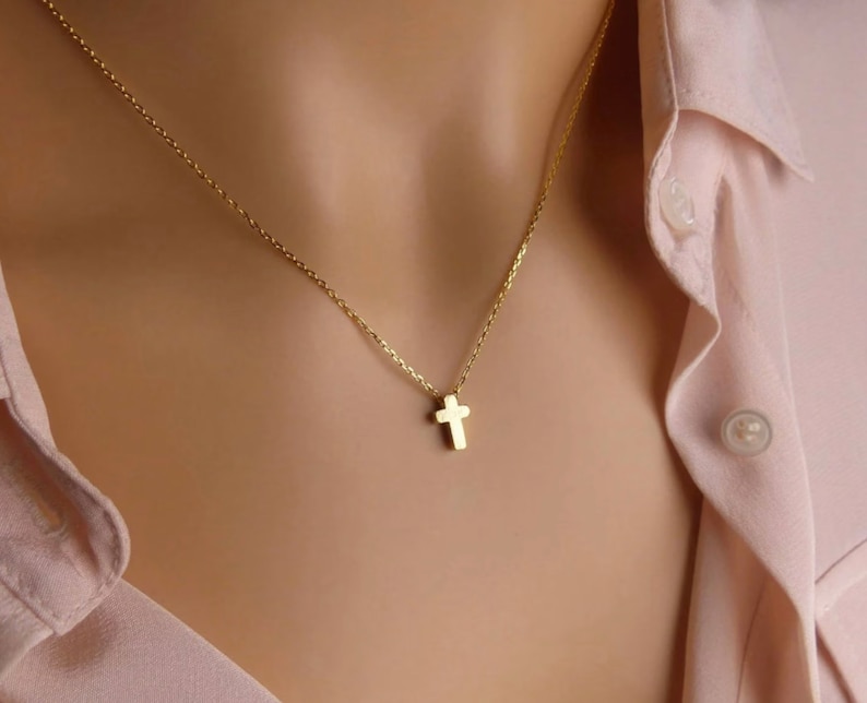 Puede incluir: Un delicado collar de cadena dorada con un peque&ntilde;o colgante de cruz simple.