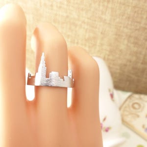 Puede incluir: Un anillo de plata con un dise&ntilde;o recortado de un horizonte de ciudad. El anillo se lleva en un dedo.