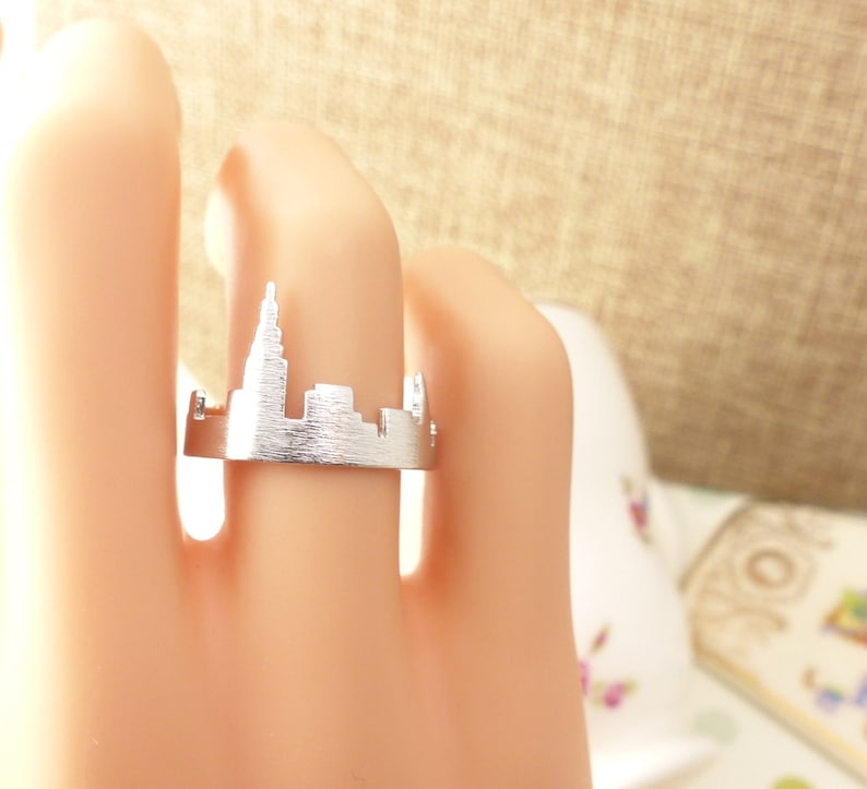 Puede incluir: Un anillo de plata con un dise&ntilde;o recortado de un horizonte de ciudad. El anillo se lleva en un dedo.