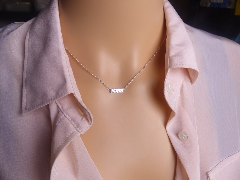 May include: A silver necklace with a delicate chain and a small pendant that says "BOSS" in block letters.