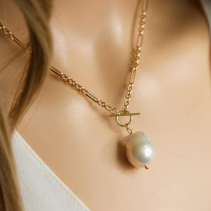 Pode incluir: Um colar de corrente de ouro com um grande pingente de pérola barroca de cor branco-creme. O colar tem um fecho de trava.