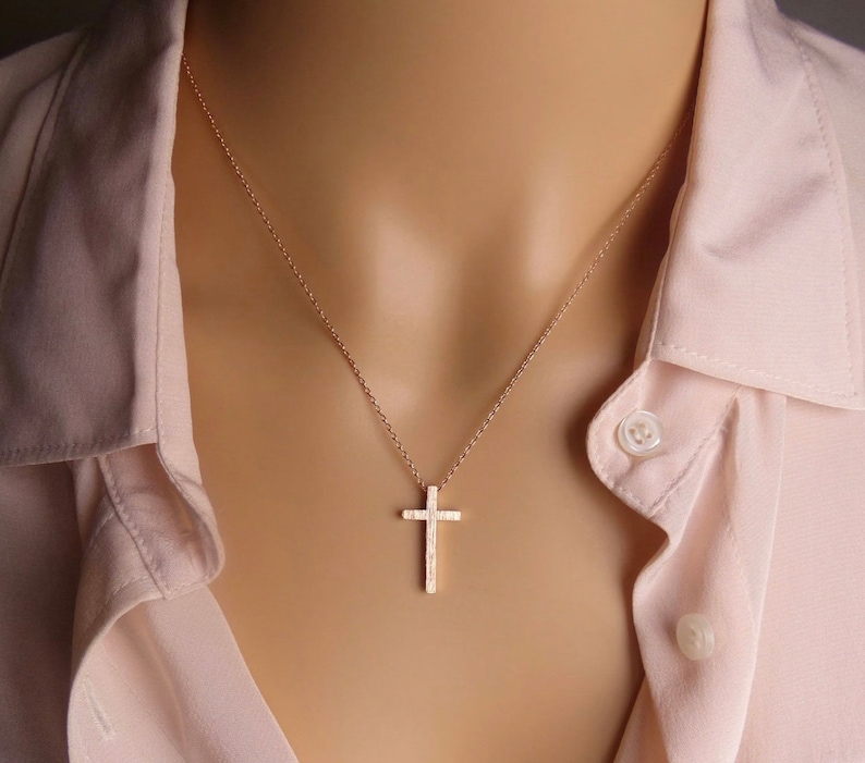 Puede incluir: Un delicado collar de cadena dorada con un peque&ntilde;o colgante de cruz texturizado.