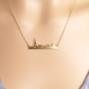 May include: A gold necklace with a delicate chain and a pendant shaped like the Paris skyline. The pendant features the Eiffel Tower and other iconic buildings.