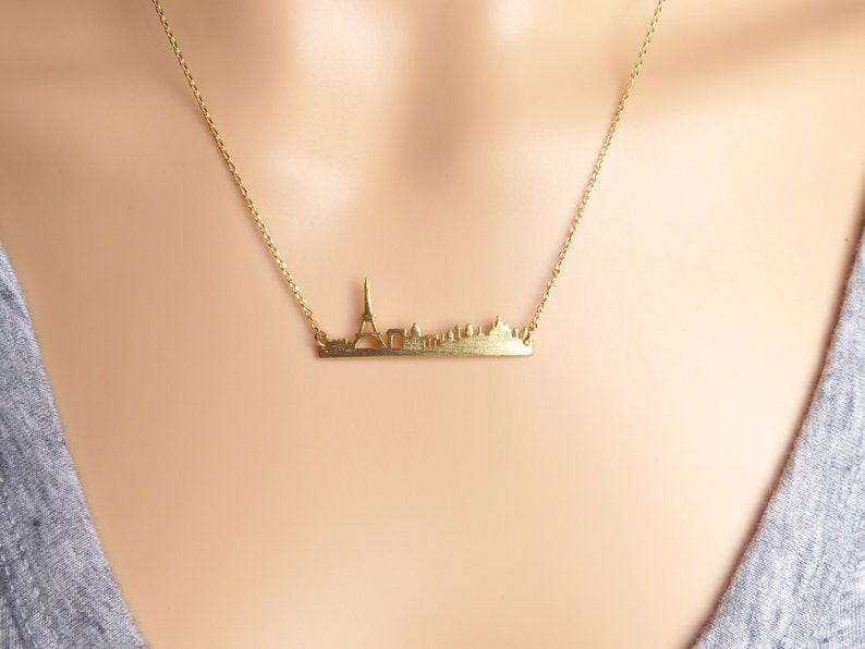 May include: A gold necklace with a delicate chain and a pendant shaped like the Paris skyline. The pendant features the Eiffel Tower and other iconic buildings.