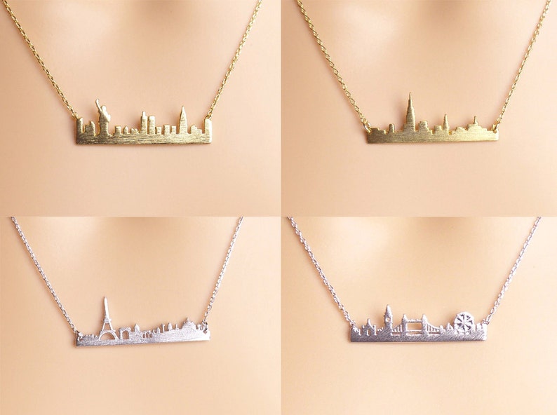 May include: Four necklaces with city skyline pendants. The top left necklace features a gold New York City skyline pendant. The top right necklace features a gold London skyline pendant. The bottom left necklace features a silver Paris skyline pendant. The bottom right necklace features a silver London skyline pendant.