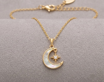Puede incluir: Un collar de tono dorado con un colgante de media luna incrustado con nácar blanco iridiscente. Un pequeño dije de estrella de cuatro puntas con una piedra clara y brillante cuelga dentro de la curva de la luna. La cadena incluye un broche.