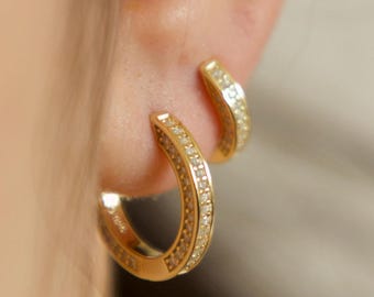 May include: A pair of gold hoop earrings with a row of small clear stones around the edge.