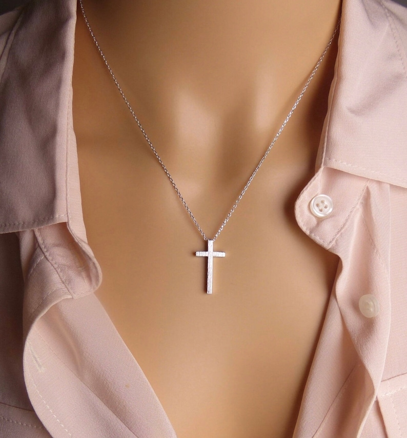 Puede incluir: Un collar de cadena de plata con un peque&ntilde;o colgante de cruz de plata texturizado.
