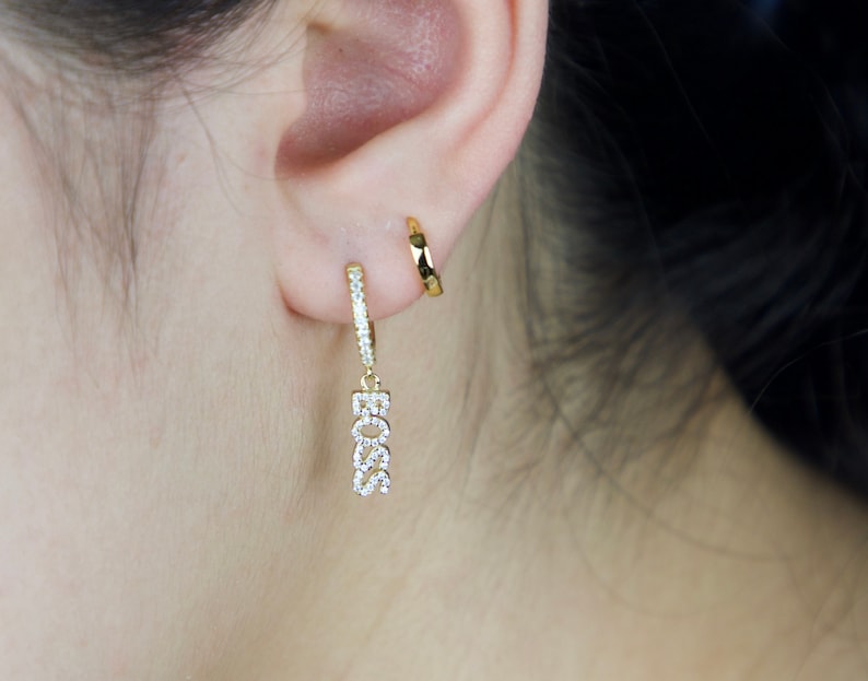 May include: Gold hoop earrings with a dangling charm that says "BOSS" in sparkly rhinestones.
