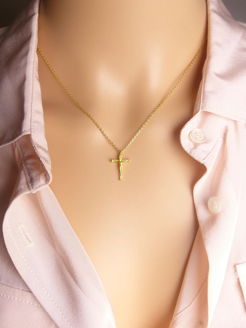 Puede incluir: Un collar de cadena dorada con un peque&ntilde;o colgante de cruz dorada. La cruz presenta un dise&ntilde;o detallado de una figura humana.