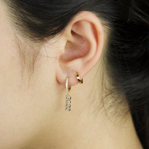 May include: Gold hoop earrings with a dangling charm featuring a row of small cubic zirconia stones.