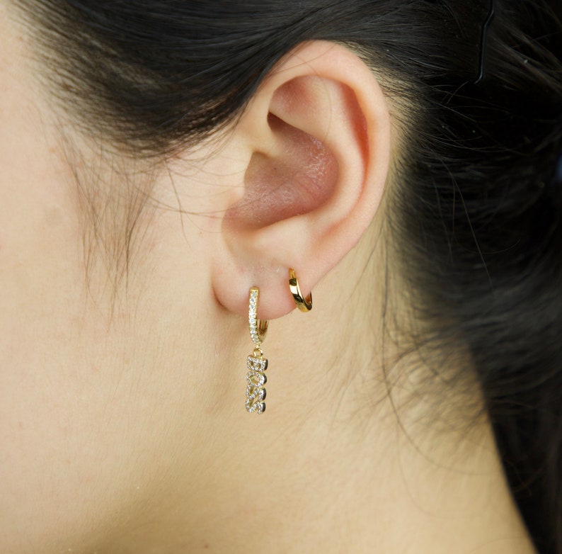 May include: Gold hoop earrings with a dangling charm featuring a row of small cubic zirconia stones.