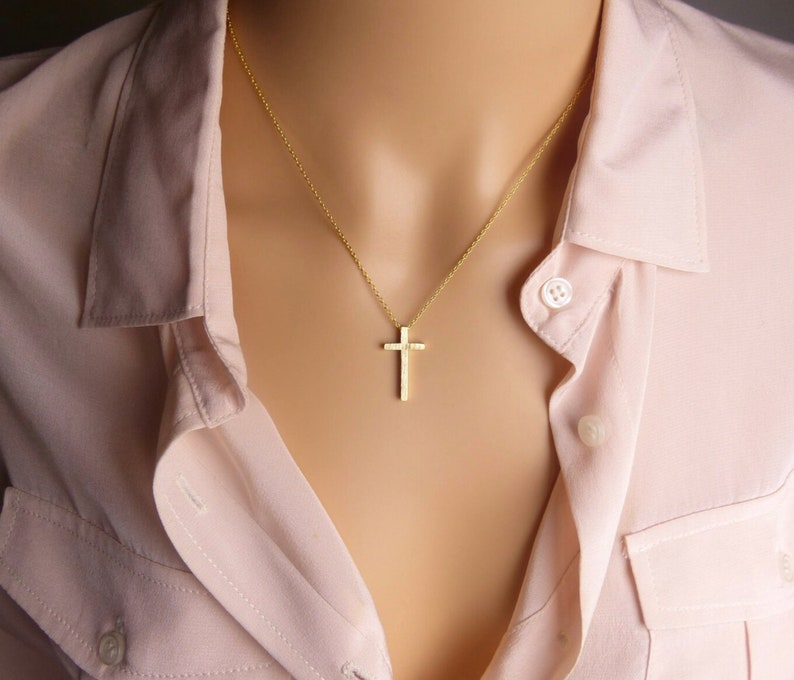 Puede incluir: Un collar de cadena de oro con un peque&ntilde;o colgante de cruz de oro texturizado.