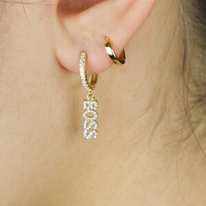 May include: Gold hoop earrings with a dangling charm that says "BOSS" in sparkly rhinestones.