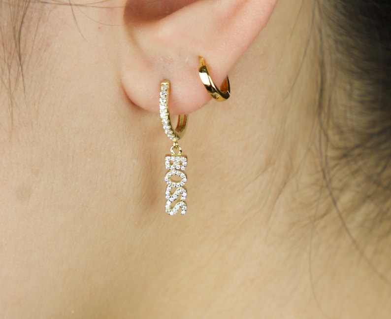 May include: Gold hoop earrings with a dangling charm that says "BOSS" in sparkly rhinestones.