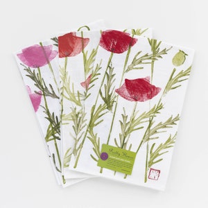 May include: Set of three white flour sack dish towels with a floral print of red and pink poppies and green leaves. The towels have a label that reads "Pretty Hours Flour Sack Dish Towel".