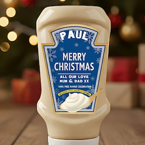 Może przedstawiać: Kremowa butelka z przyprawami z niebieską etykietą z napisem "PAUL MERRY CHRISTMAS". Etykieta zawiera również płatki śniegu i tekst "ALL OUR LOVE MUM & DAD XX". Wir w łyżce pokazano wir przyprawy. Butelka ma białą nasadkę.