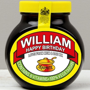 May include: A dark brown glass jar with a yellow lid and a personalized label. The label features a red banner with the text WILLIAM HAPPY BIRTHDAY, LOVE FROM MUM & DAD XX, and a graphic of a yellow pot with the word MARMITE printed on it.