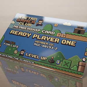 Puede incluir: Una tarjeta de membresía rectangular con un paisaje de videojuego pixelado con cielo azul, colinas verdes y un castillo. El texto incluye RETRO GAMER CLUB, MEMBERSHIP CARD, READY PLAYER ONE, VALID: FOR LIFE, MEMBER ID: RGC-88193-Z y UNLOCKING THE CLASSICS.
