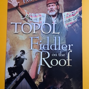 May include: A promotional poster for "Fiddler on the Roof" featuring Topol. The poster has a warm color palette with the title text in large, bold letters. A man with a beard is featured with his arms raised. A violinist is also featured.