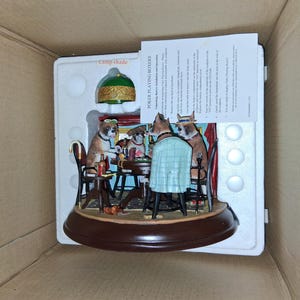 May include: A decorative figurine depicting boxer dogs playing poker around a table. The scene includes a green lampshade, chairs, and a detailed poker table setting. The figurine is in a white box.