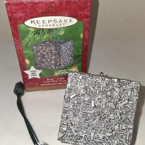 May include: A silver-colored Borg Cube ornament with a complex, geometric design. The ornament is from the Star Trek Voyager series and includes a green power cord. The box reads "Keepsake Ornament".