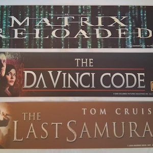May include: Three movie promotional banners. The top banner reads "MATRIX RELOADED" with a green and black background. The middle banner says "THE DA VINCI CODE" with actors' faces. The bottom banner says "THE LAST SAMURAI".
