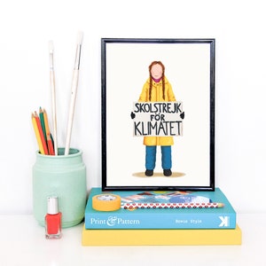 Puede incluir: Una ilustraci&oacute;n enmarcada de una persona con un impermeable amarillo sosteniendo un cartel que dice "SKOLSTREJK FOR KLIMATET". La ilustraci&oacute;n est&aacute; sobre un fondo blanco. El marco es negro.
