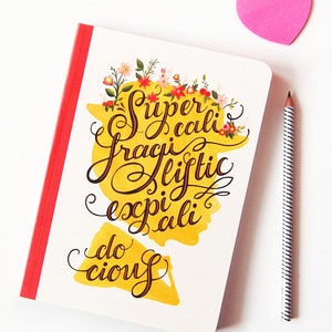 May include: A yellow notebook with a red spine and a floral design. The notebook has the words "Supercalifragilisticexpialidocious" written in black cursive.
