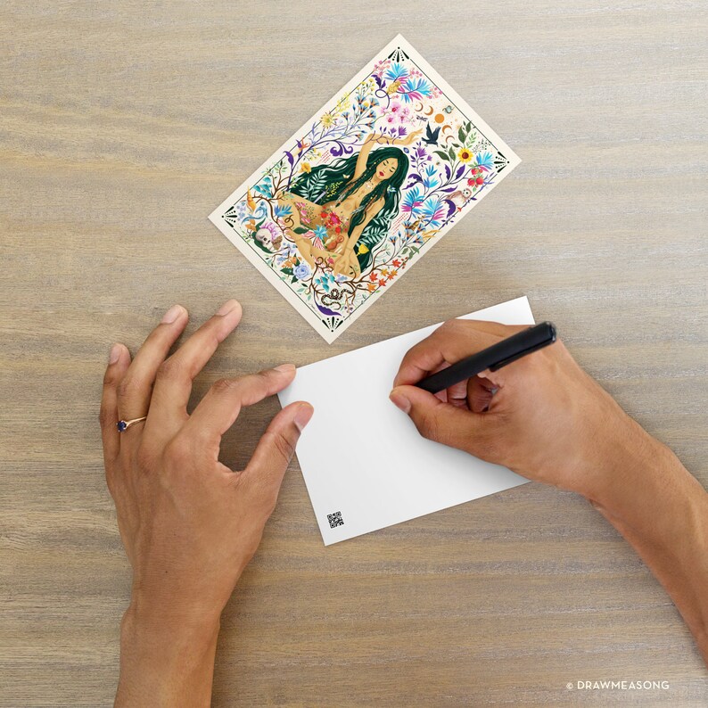 May include: A postcard featuring a colorful illustration of a woman surrounded by flowers and other botanical elements. The woman is wearing a floral crown and has long, flowing hair. The postcard is blank on the back, ready for writing.