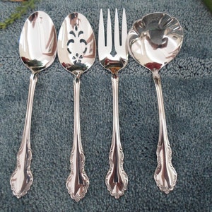 May include: Set of four silver-plated serving utensils, including a slotted spoon, a serving spoon, a serving fork, and a ladle. The utensils have ornate handles with a floral design.