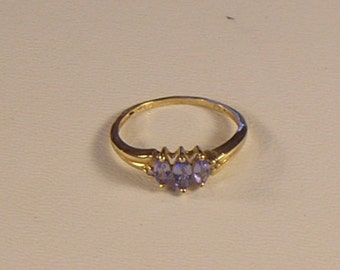 May include: A gold ring with three purple gemstones set in a prong setting.