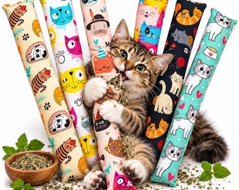May include: A brown tabby cat holding a long, cylindrical fabric catnip toy. The toy is one of several patterned tubes featuring colorful cartoon cat illustrations, including orange, pink, blue, and black designs, scattered with loose dried catnip.