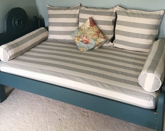 May include: A blue daybed with a gray and white striped mattress and pillows. The daybed has two bolster pillows and three square pillows. One square pillow has a floral pattern.