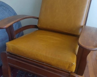 May include: A brown leather armchair with wooden arms and legs. The chair has a deep seat and a high back.