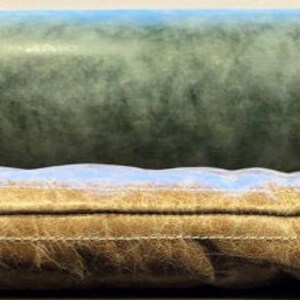 May include: Close-up of a brown leather sofa cushion with a light blue seam and a light blue and green fabric backing.