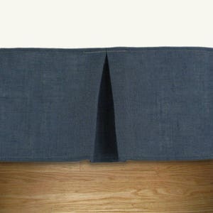 May include: A dark blue bed skirt with a single pleat in the center. The skirt is made of a textured fabric and is shown against a light wood background.