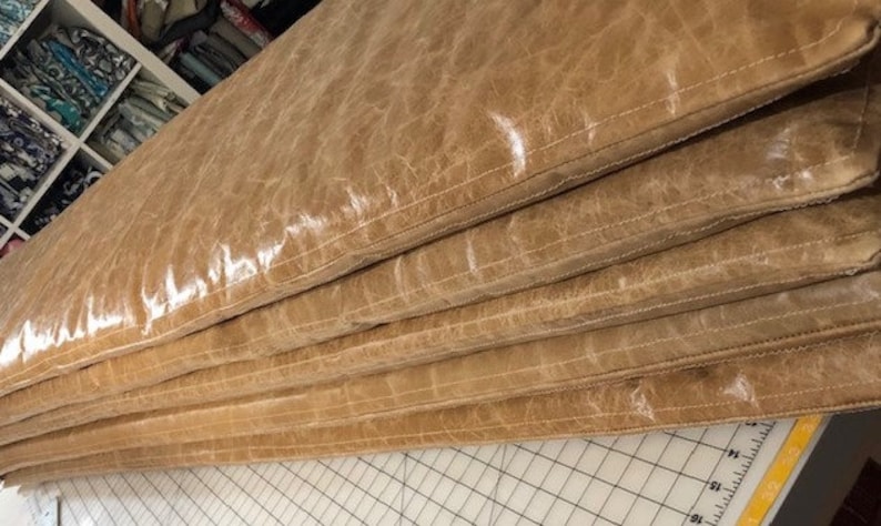 May include: Stack of five brown leather cushions with a subtle sheen. The cushions are stitched together with a light brown thread.