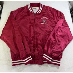 May include: A maroon satin varsity jacket with white striped ribbed trim on the collar and cuffs. The front features a snap-button closure and an embroidered logo with the text Alabama A Roll Tide. A Chalk Line brand label is inside the collar.