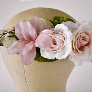 Puede incluir: Una corona floral con grandes rosas rosas p&aacute;lidas y blancas, y flores rosas y blancas m&aacute;s peque&ntilde;as. La corona se coloca sobre un fondo neutro, destacando los delicados detalles de las flores artificiales.