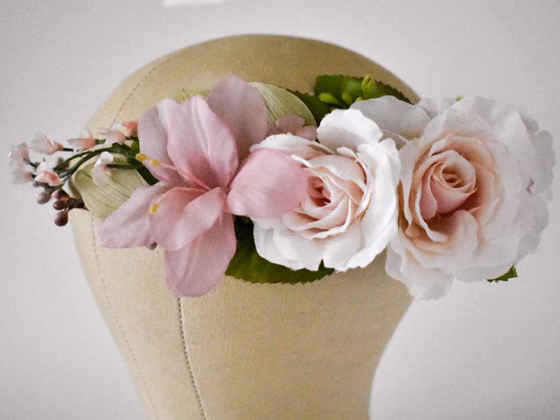 Puede incluir: Una corona floral con grandes rosas rosas p&aacute;lidas y blancas, y flores rosas y blancas m&aacute;s peque&ntilde;as. La corona se coloca sobre un fondo neutro, destacando los delicados detalles de las flores artificiales.