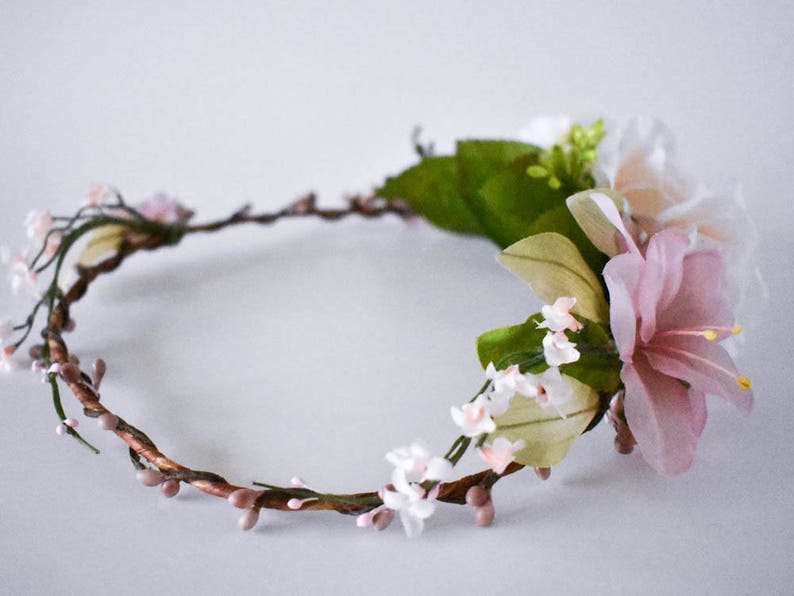 Puede incluir: Una corona floral con un dise&ntilde;o delicado. La corona est&aacute; hecha de vides marrones y retorcidas adornadas con peque&ntilde;os capullos rosados y racimos de flores blancas y rosas. Tambi&eacute;n hay grandes flores rosas y blancas con estambres amarillos.